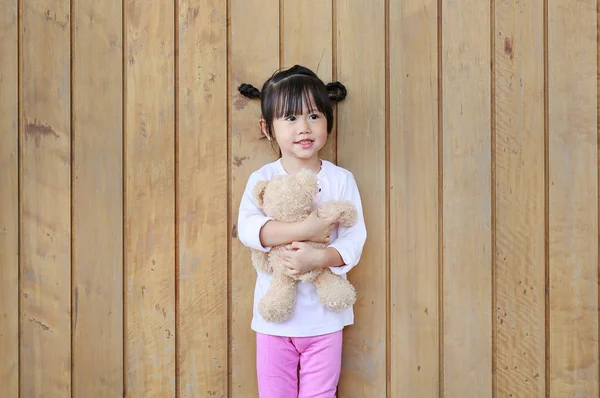 Retrato de pie linda niña y abrazo osito de peluche contra la pared de madera tablón — Foto de Stock