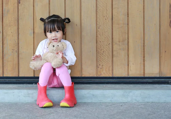 Retrato de menina bonito sentar e abraçar ursinho de pelúcia contra a parede da prancha de madeira — Fotografia de Stock
