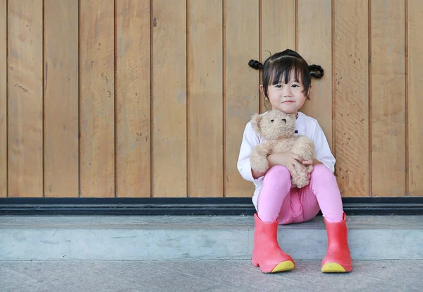 Retrato de menina bonito sentar e abraçar ursinho de pelúcia contra a parede da prancha de madeira — Fotografia de Stock