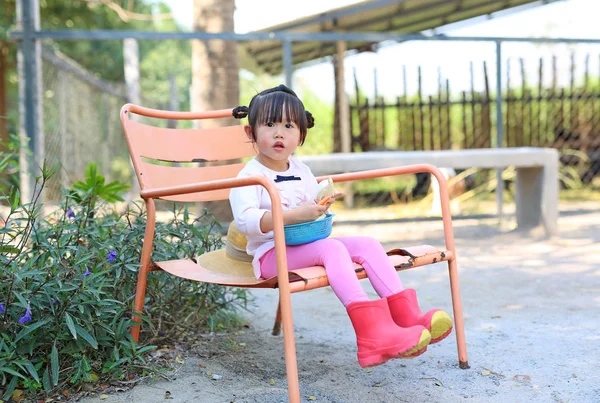 Pouco menina asiática sentada na cadeira ao ar livre na fazenda com comida vegetal para um animal . — Fotografia de Stock