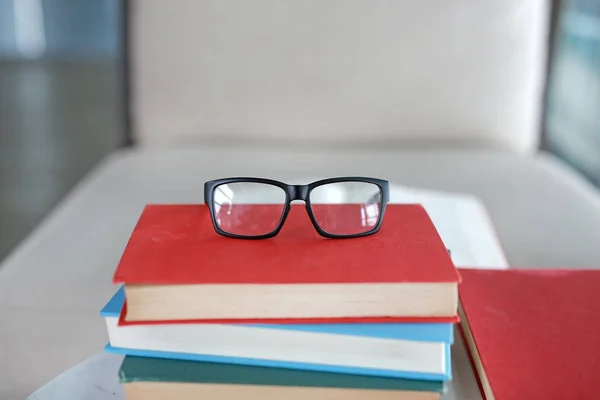 Stack of textbooks on desk with glasses on the top in library room, Education concept background.