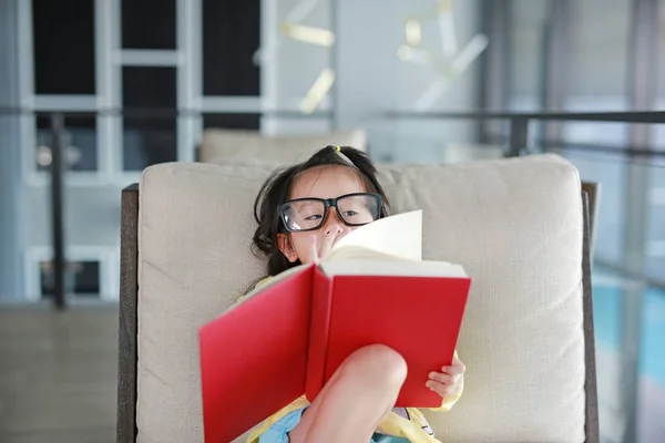 Niña con gafas leyendo libro en la biblioteca, concepto de educación . — Foto de Stock