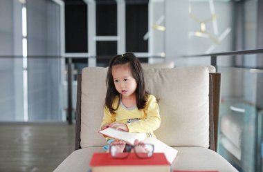 Küçük çocuk kız okuma kitabı kitaplığında, eğitim kavramı.