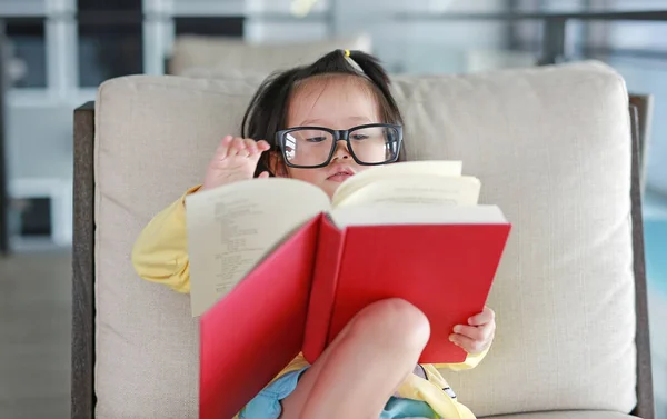 Kind meisje met bril lezen boek in bibliotheek, onderwijs concept. — Stockfoto