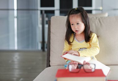 Küçük çocuk kız okuma kitabı kitaplığında, eğitim kavramı.