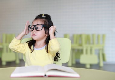 Zeki küçük çocuk kız çocuk odası bir kitap okuma gözlüklü.