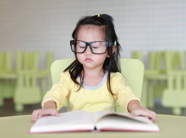 Zeki küçük çocuk kız çocuk odası bir kitap okuma gözlüklü.