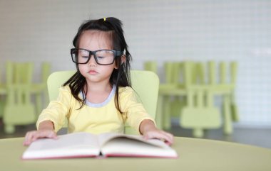 Zeki küçük çocuk kız çocuk odası bir kitap okuma gözlüklü.