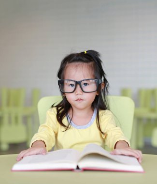 Zeki küçük çocuk kız çocuk odası bir kitap okuma gözlüklü.