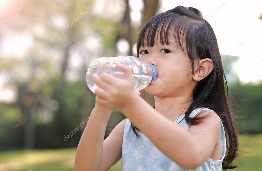 Close Up little girl drinking water from bottle in the park. Portrait outdoor.