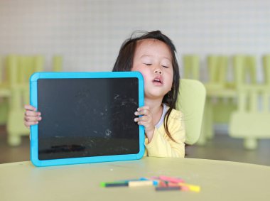 Boş yazı tahtası odasında tutan şirin Asyalı çocuk kız.