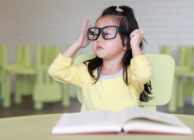 Zeki küçük çocuk kız çocuk odası bir kitap okuma gözlüklü.