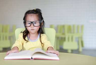 Zeki küçük çocuk kız çocuk odası bir kitap okuma gözlüklü.