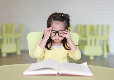 Zeki küçük çocuk kız çocuk odası bir kitap okuma gözlüklü.