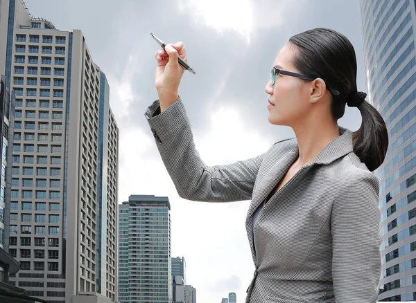 年轻的商业妇女使用笔写作在空气反对大厦背景 商业概念 — 图库照片
