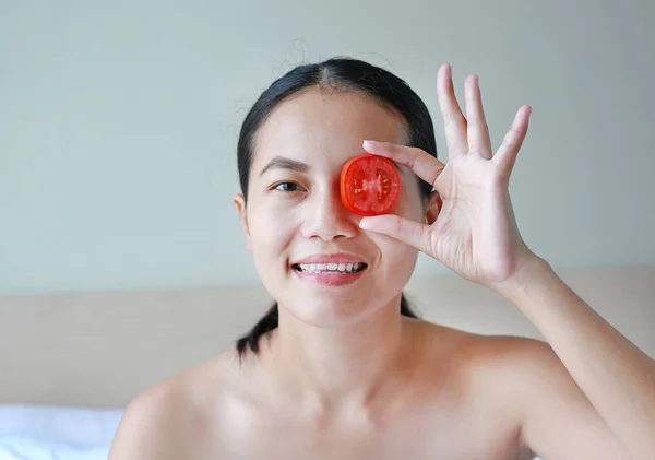 Young woman holding tomato slices on her eye, concept for skin care.