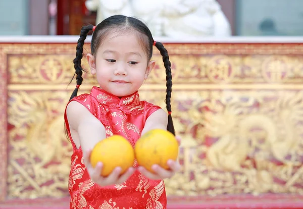Smiling asian kid girl in traditional Chinese dress with holding sacred Orange at chinese temple in bangkok thailand, Chinese new year concept.
