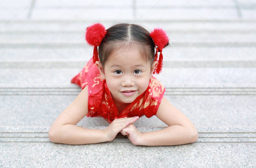 Happy little Asian child girl wearing red cheongsam with greeting gesture celebration for Chinese New Year at chinese temple in thailand.