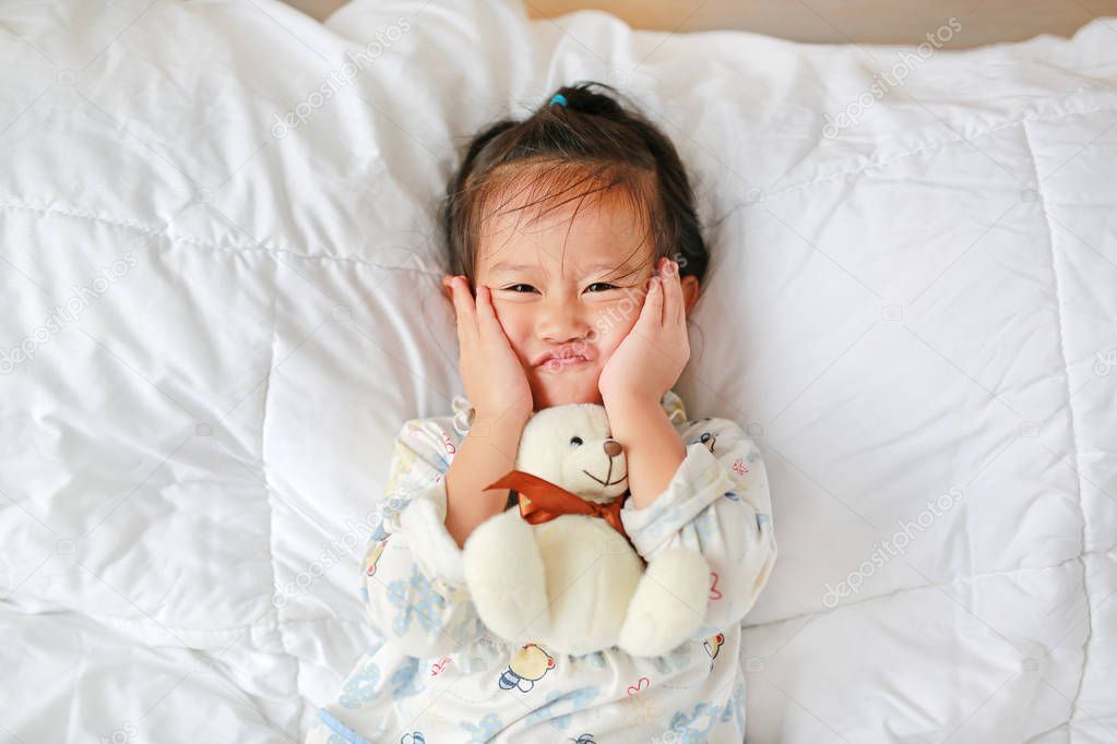 Funny face asian little girl with teddy bear lying on bed