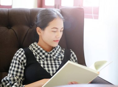 Genç Asyalı kadın kütüphanede kitap okumak.