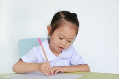 Asyalı çocuk okulda kalem masanın üzerine yazma ile Tekdüzen beyaz arka plan üzerinde izole.