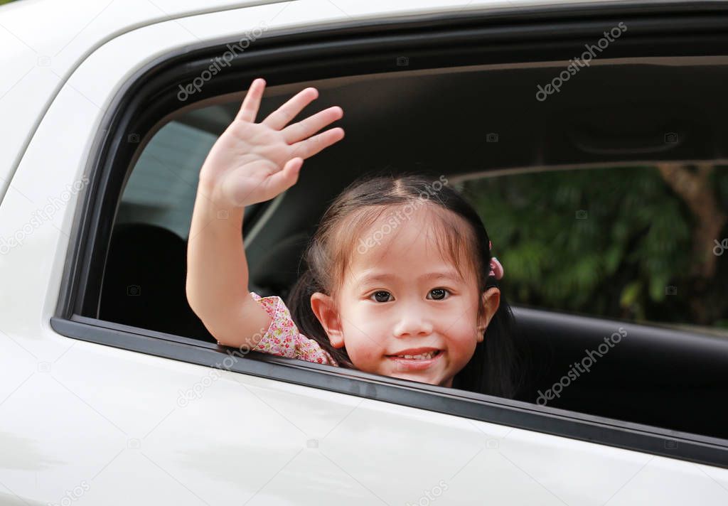 Cute asian girl in a backseat of a car waving goodbye.