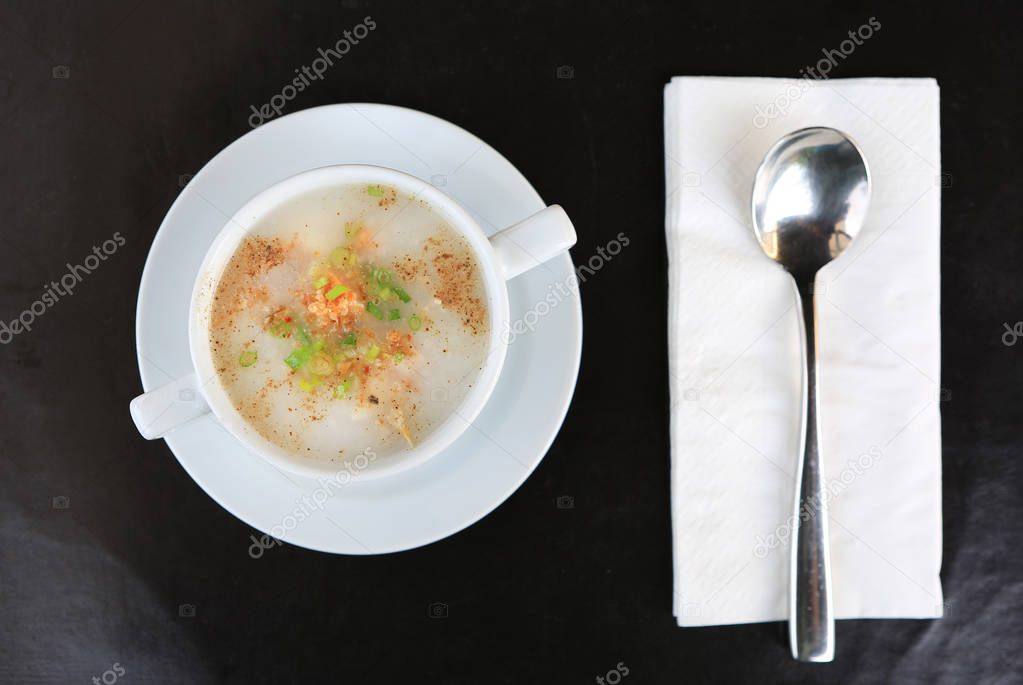 Top view Traditional Thailand porridge rice gruel in cup on black leather plate with spoon and tissue.