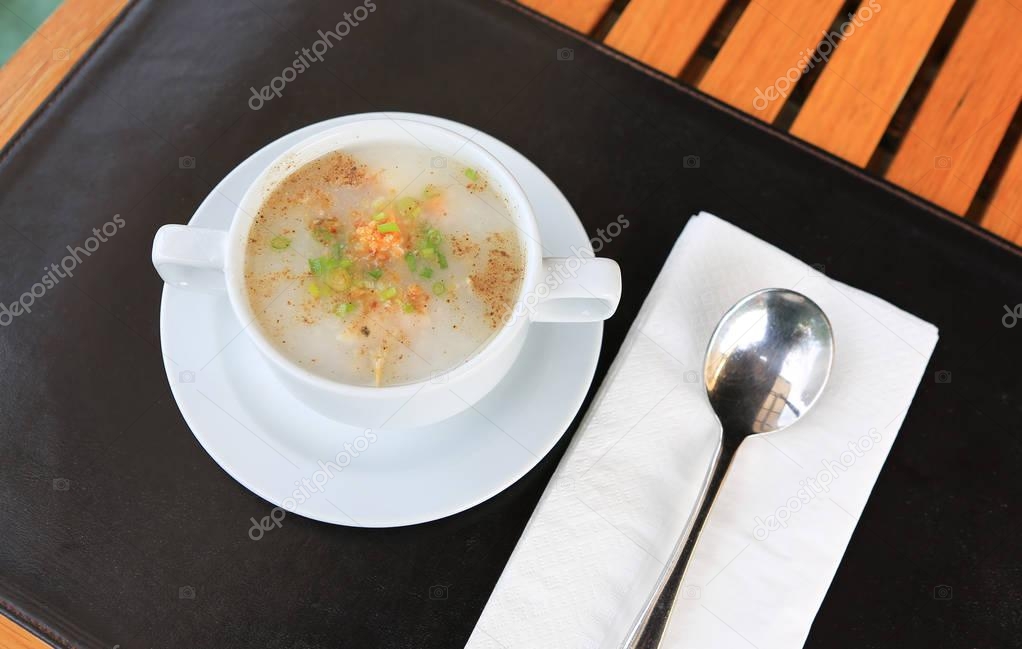 Traditional Thailand porridge rice gruel in cup on wooden table with spoon and tissue.