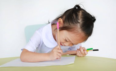 Asyalı çocuk okulda kalem masanın üzerine yazma ile Tekdüzen beyaz arka plan üzerinde izole.