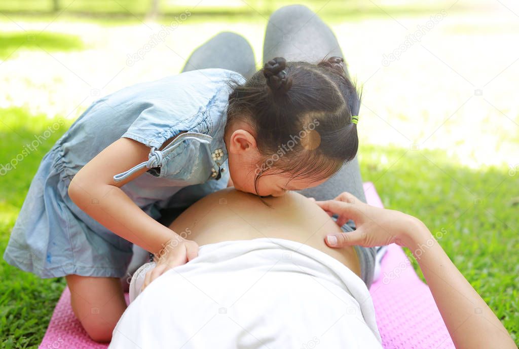 Happy child kissing belly of pregnant women in the garden