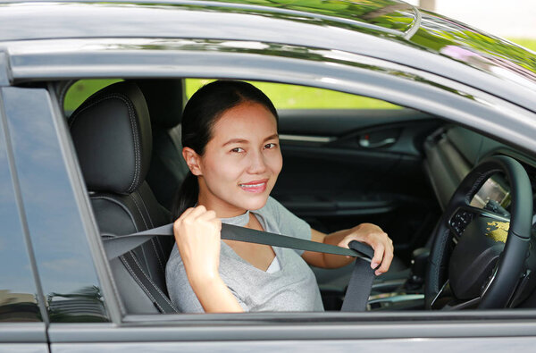 Portrait of a young asian woman inside a car using safety belt before drive