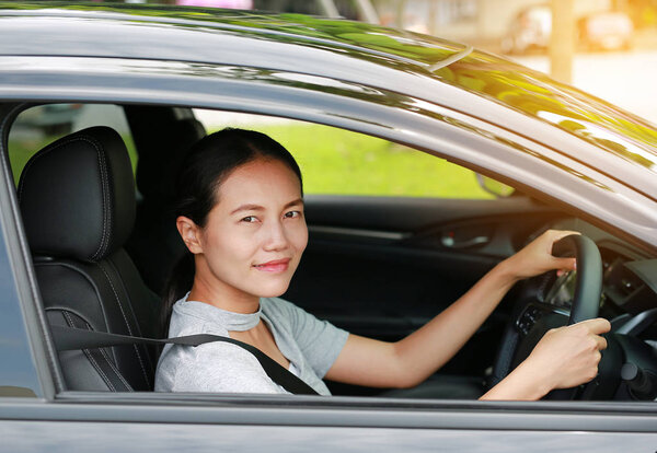 Beautiful asian woman driving a car with looking camera and smiling.