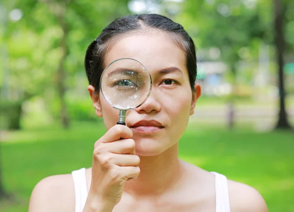 Asian woman with a magnifying glass on eye in the garden