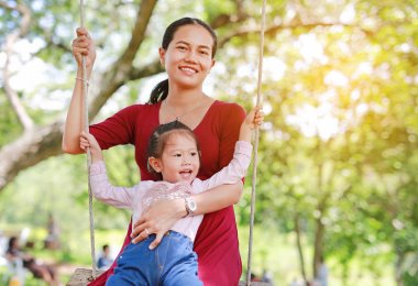 Mutlu Asya anne ve kızı, güneş ışınları ile bahçede sallanan yalan.
