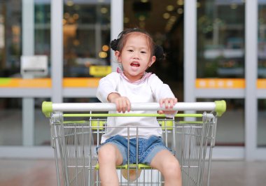 Aile içinde belgili tanımlık çarşı alışveriş sırasında arabası içinde oturan küçük çocuk kız gülümseyerek.