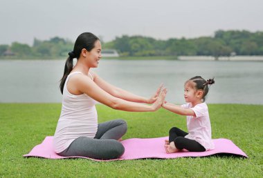 Hamile anne ve kızı genel parkta yoga yaparken.