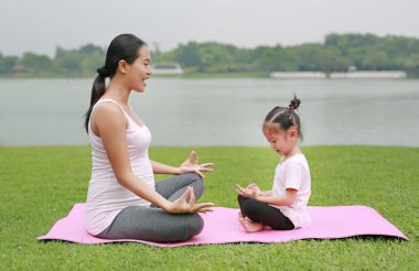 Hamile anne ve kızı genel parkta yoga yaparken.