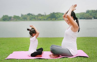 Hamile anne ve kızı genel parkta yoga yaparken.