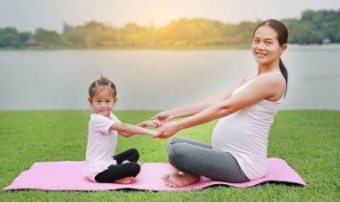 Hamile anne ve kızı genel parkta yoga yaparken.