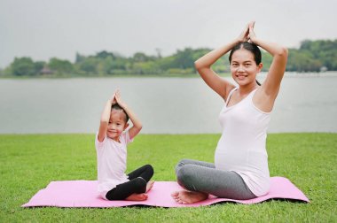 Hamile anne ve kızı genel parkta yoga yaparken.