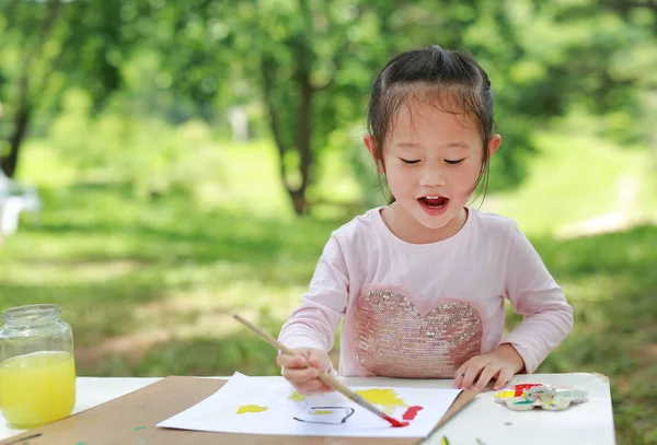 テーブルの上に座って 緑豊かな庭園 アート紙にブラシでペイントに喜んでいる子供 — ストック写真