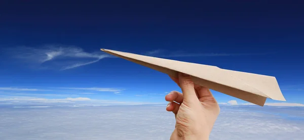 Brown aircraft rocket paper in hand on puffy cloud sky background.