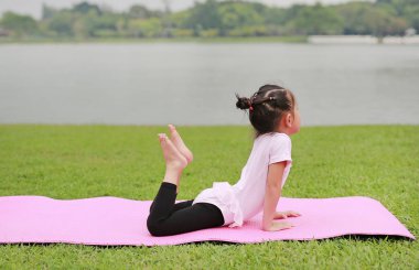 Genel parkta yoga yaparken sevimli küçük Asyalı çocuk kız.