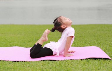 Genel parkta yoga yaparken sevimli küçük Asyalı çocuk kız.
