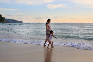 Siluet hamile anne ve kızı birlikte gün batımında sahilde yürüyüş.