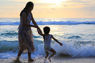 Siluet anne ve kızı gün batımında sahilde oynarken.