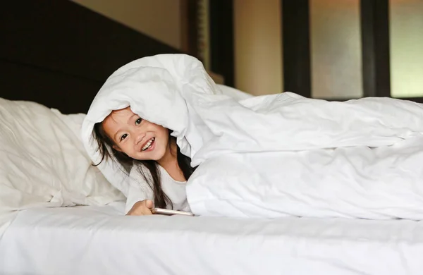 Szczęśliwa Dziewczynka Azjatyckich Leżącego Pod Koc Łóżku Patrząc Kamery — Zdjęcie stockowe