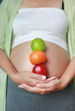 Yeşil-Kırmızı elma ve portakal meyve karnı holding ve karnı dokunmadan hamile kadın.