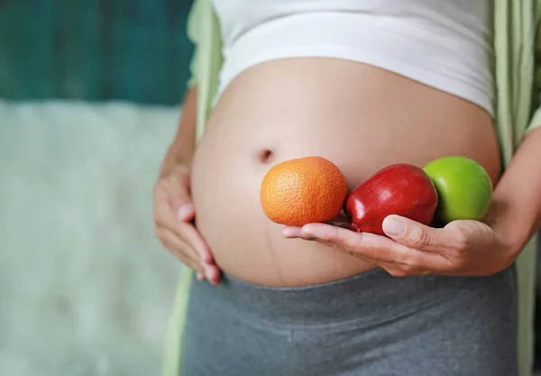 孕妇抱着绿红苹果和橙果在她的肚子上抚摸她的腹部 — 图库照片