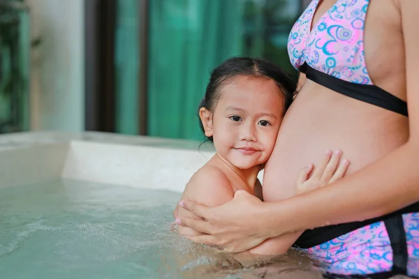 Little child girl listening belly of pregnant women in hot tub.